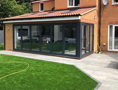 Anthracite grey folding glazed panels across a single-storey brick extension with tiled roof