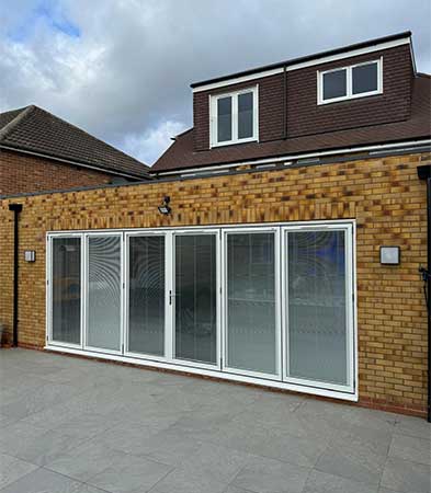 Six-panel white folding glazed system on a yellow brick extension facing a paved patio