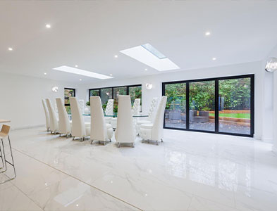 White dining room with black-framed sliding glazed panels and skylights overlooking a garden