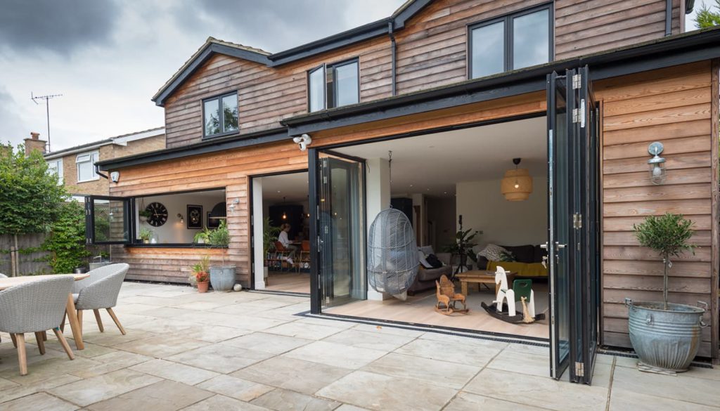 Timber-clad house with open anthracite aluminium bifold doors onto a paved patio