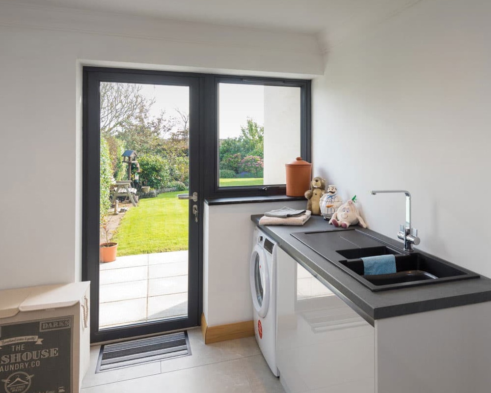 Utility room with open anthracite aluminium back door and side window overlooking a garden