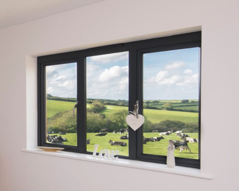 Interior view through a slim anthracite aluminium triple window onto green farmland