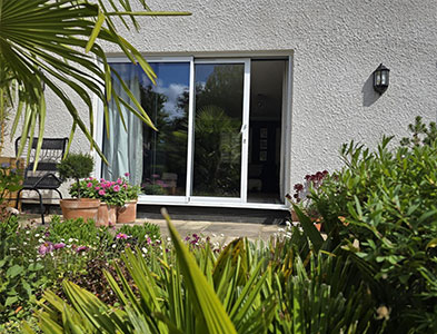 White-framed glazed panels on a rendered wall viewed through a lush planted garden