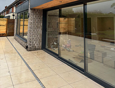 Wide anthracite glazed panels under a timber soffit beside a cream tiled patio