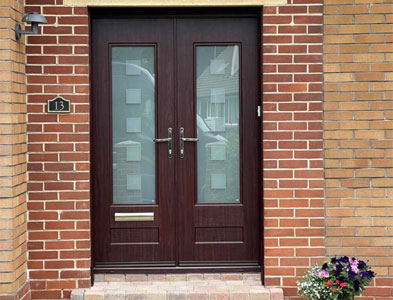 Dark rosewood double entrance with patterned glazed panels in a red brick porch