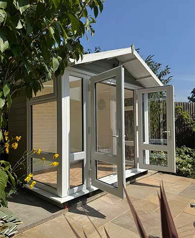 Small cream garden pod with open French doors and full-height panes on a stone patio