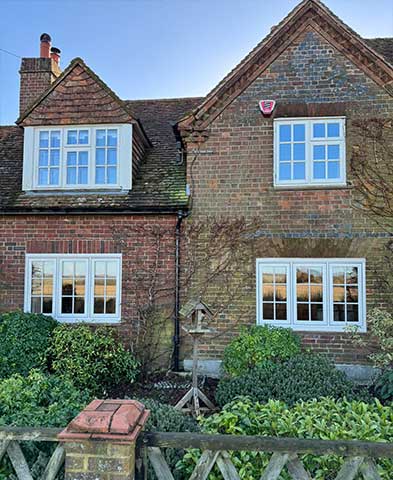 White timber-effect casement units with bars across the front of a period brick cottage