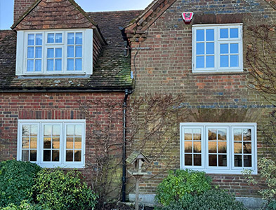Cream casement frames with multi-pane glazing on a traditional brick cottage exterior surrounded by greenery