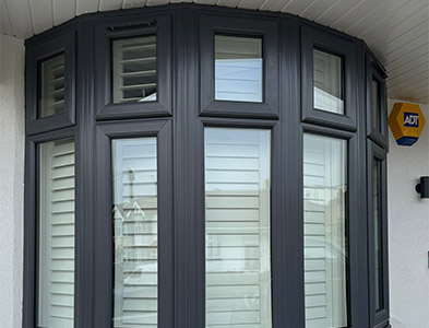 Anthracite grey curved bay-style frames with plantation shutters on a rendered house exterior